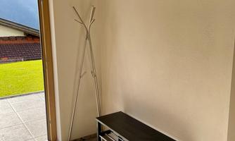 A bright entrance area with a black bench and a minimalist coat rack. The door opens to a beautiful view outside.