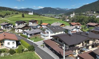 A picturesque village view with several beautiful houses and green fields. In the background, mountains and a blue sky can be seen.