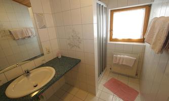 A modern bathroom with a sink, a mirror, and a shower. The walls are tiled and there is a window that lets in natural light.