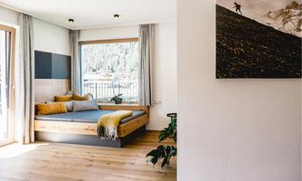 A bright and modern bedroom with wooden details and a cozy lounge chair. Through the window, there is a beautiful view of nature.