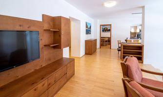 A modern living space with wooden shelves and a television. The room is bright and inviting with an open dining area in the background.