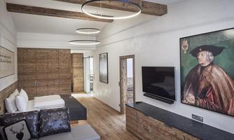 A modern room with wooden flooring and stylish furniture. A large painting hangs on the wall, and there are cozy seating areas.
