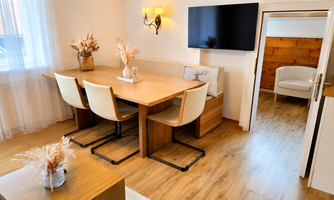 A bright dining room with a wooden log table and comfortable chairs.  
A TV is hanging on the wall and the room is adorned with stylish decorations.
