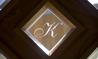 A wooden sign with an elegant, engraved letter "K" in the center. The frame has a diamond shape and features a simple, modern style.