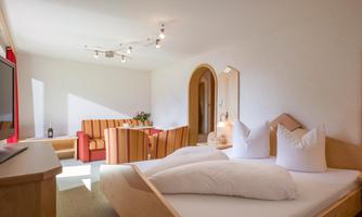 A bright room with a double bed and cozy armchairs. Large windows provide plenty of light and an inviting atmosphere.