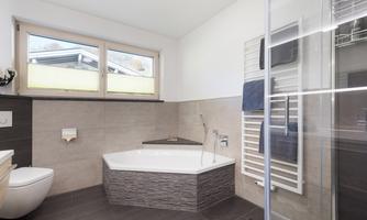 A modern bathroom with a corner bathtub and a glass shower. Large windows provide plenty of daylight.