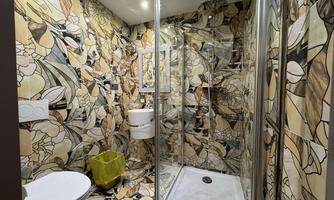 A modern bathroom with a colorful wall tile pattern. There is a shower, a toilet, and a sink.