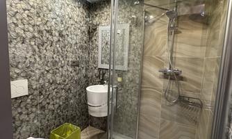 A modern bathroom with a glass shower and stylish, patterned tiles. A small yellow trash can and a sink complete the decor.