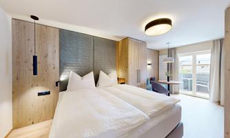 A modern bedroom with a large double bed and wooden paneling. The room has large windows that let in plenty of daylight.
