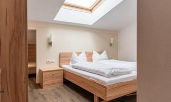 A bright bedroom with a large double bed and wooden furniture. The room has a skylight and a minimalist, modern style.