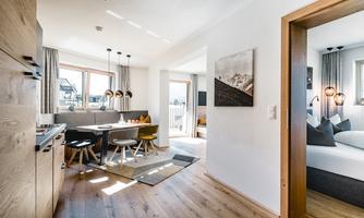 A modern apartment with a cozy dining area and an open kitchen. Large windows provide plenty of daylight and a friendly atmosphere.