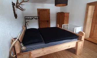 A cozy bedroom with a wooden bed and black bedding. The decor is in rustic style with a carpet and a chandelier.