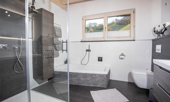 A modern bathroom with a shower and a bathtub. Large windows provide daylight and a view of the greenery.
