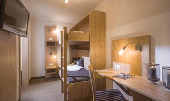 A cozy room with a bunk bed and a desk. The walls and furniture are made of wood, and there is modern lighting as well as a television.