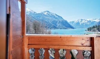 A beautiful view from a balcony of a clear lake and snow-capped mountains. The landscape is peaceful and inviting.