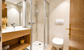 A modern bathroom with a glass sliding door and a shower. The room has bright walls and is equipped with wooden shelves.