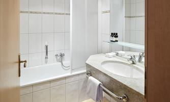 A modern bathroom with a bathtub and a shower. There is a large mirror and elegant, bright tiles.