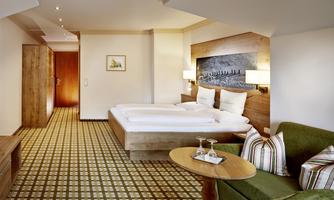 A modern hotel room with a large bed, a cozy seating area, and wooden decorations. The warm colors create an inviting atmosphere.
