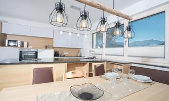 Modern kitchen with wooden details and large windows. The dining area is elegantly set with crockery and a decorative centerpiece.