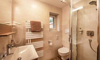Modern bathroom with shower, sink, and toilet. The walls are light tiled and a window provides natural light.