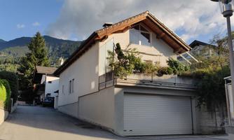 A modern house on a quiet street, surrounded by trees and mountains. The sky is clear and the atmosphere is peaceful.