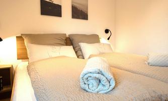 A cozy bedroom with two separate beds. The bedding is neutral, and a rolled towel lies on the bed.