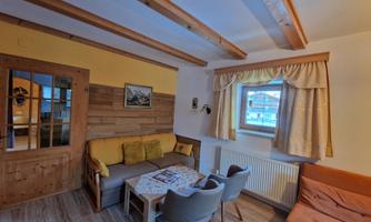 A cozy living room with wooden furniture and a large window. The decor is rustic and inviting.