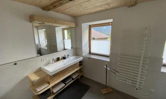 A modern bathroom with a wooden ceiling and an elegant washbasin. The window lets in plenty of daylight and offers a view of the outdoors.
