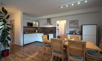 Modern kitchen with wooden details and a dining area. Large table with chairs and a green plant in the room.