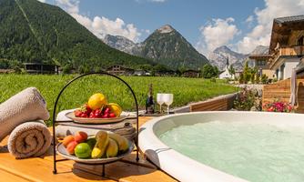 A relaxing hot tub with a view of the mountains. Fresh fruit and two glasses are next to the hot tub.