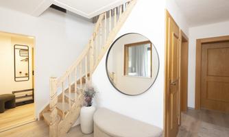 A bright entrance area with a wooden staircase and a round mirror. There is a modern seating area and a plant in a pot.