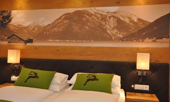 A cozy bedroom with a large bed and rustic wood design. Above the bed hangs a picture of mountains and a lake.