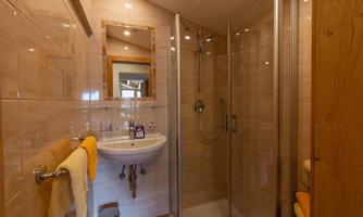 A modern bathroom with a shower, a sink, and bright tiles. Towels in yellow and a mirror are also available.