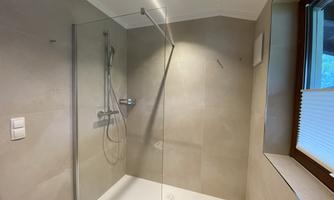 A modern shower with a glass partition and neutral tiles. Sufficient daylight from a window creates a bright atmosphere.