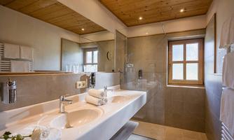 A modern bathroom with a double sink and bright wooden ceilings. Large windows provide plenty of natural light.