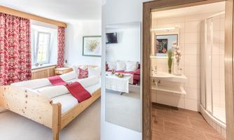 A cozy bedroom with a wooden bed and red curtains. In the background, there is a modern bathroom with a shower.