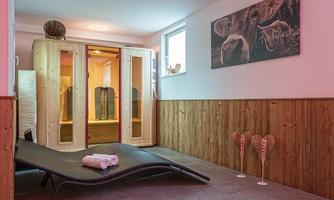 A modern wellness area with a wooden sauna and a lounge chair. The walls are clad with warm wooden panels and there are decorative elements.