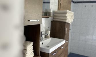 A modern bathroom with wooden cabinets and a sink. Clean, folded towels are neatly stacked.