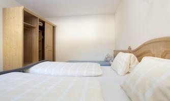 A simple bedroom with two beds and a wooden wardrobe. The walls are light, and the room feels friendly and inviting.