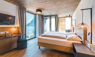 A modern bedroom with a large bed and wooden floor. The room has panoramic windows with a view of the mountains.