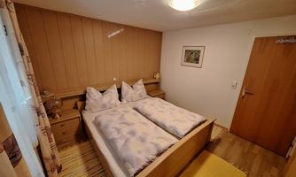 A cozy bedroom with a double bed and two pillows. The walls are in warm wood tones and there is a small carpet on the floor.