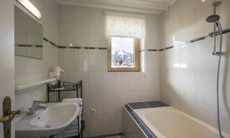 A bright bathroom with a bathtub and a sink. Through the window, you can see a picturesque mountain landscape.
