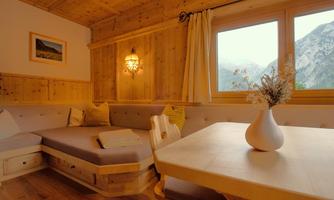 A cozy room with wooden walls and a comfortable seating area. Large windows offer a view of the mountains and allow plenty of natural light.