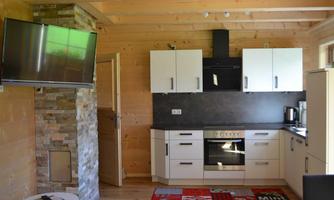 A modern kitchen in a wooden house with white cabinets and black appliances. A TV hangs on the wall and the floor is made of wood.