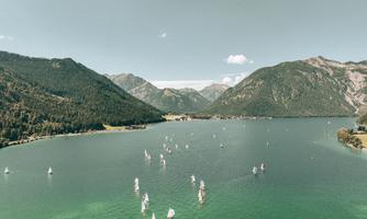 A picturesque landscape with a clear green lake and sailboats. Surrounded by tall mountains and a bright sky.
