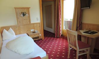A cozy hotel room with wooden paneling. There is a single bed, a table, and a television.