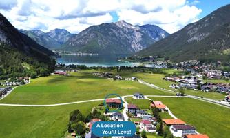 A picturesque landscape with green meadows, mountains in the background, and a clear lake. Charming residential houses complement the idyllic scene.