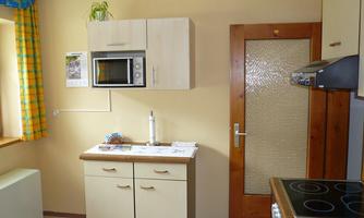 A small, modern kitchen with a microwave oven and a stove. The walls are light, and there is a window with colorful curtains.