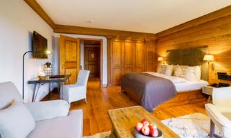 A cozy hotel room with wooden furniture and a large bed. The decor is modern and inviting, with a small desk and a comfortable seating area.