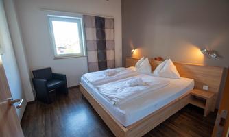 A cozy bedroom with a large bed and soft pillows. There is a chair and a window that lets in daylight.